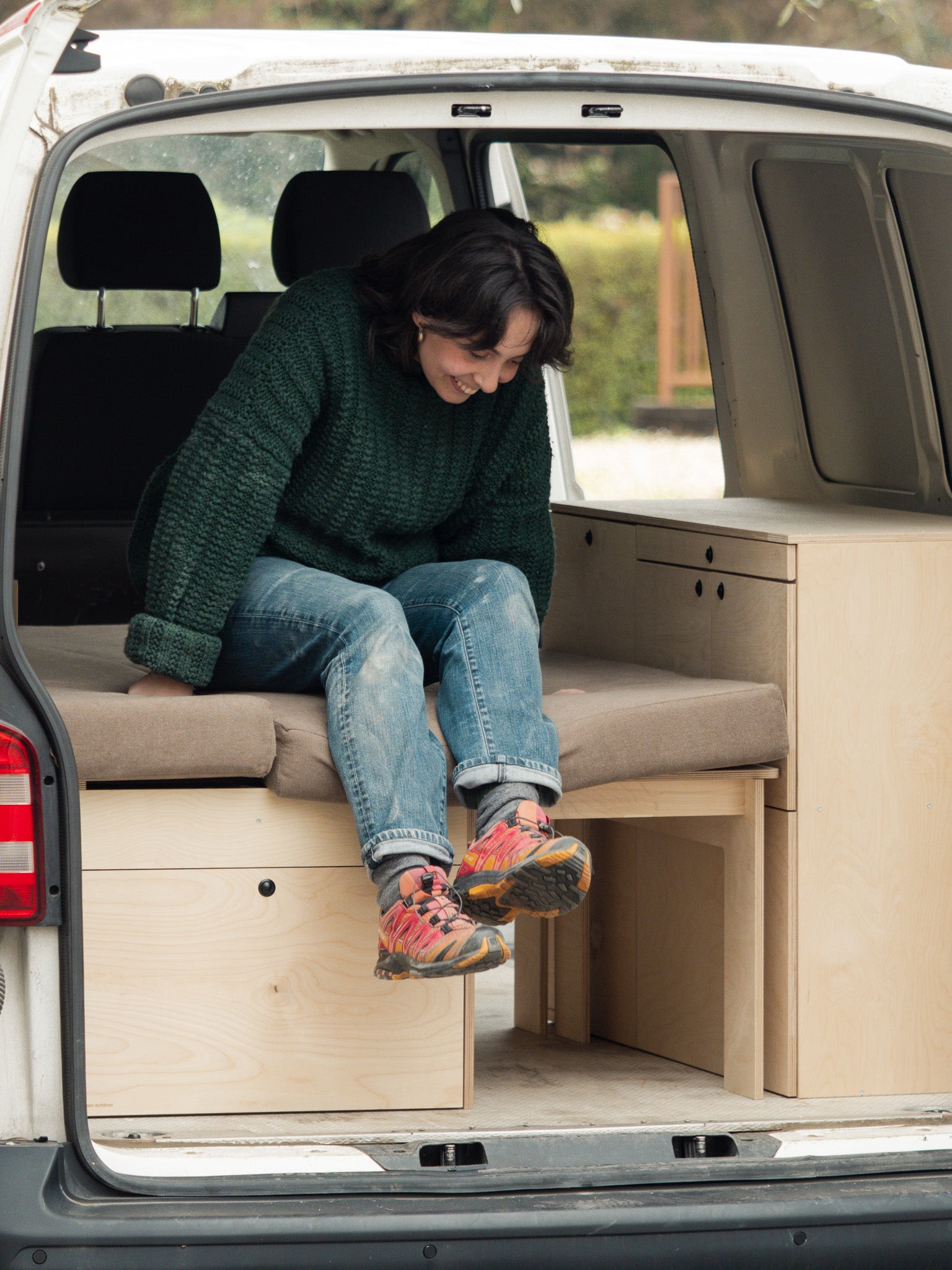 una ragazza seduta sul letto Nom Outdoor con storage S all'interno di un van T6