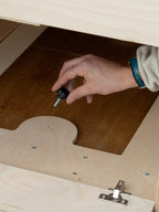 Mano che posiziona la bussola filettata del sistema di fissaggio Nom Outdoor nel pianale del furgone, componente per ancorare in modo sicuro i moduli della camperizzazione van