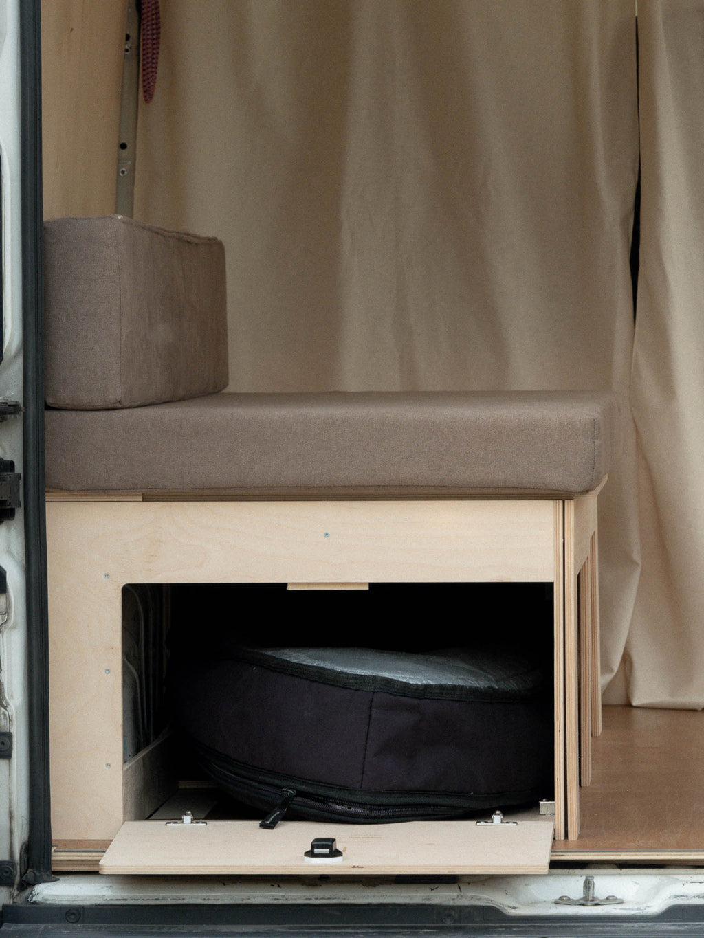 Letto Nom Outdoor in modalità divano con anta laterale aperta e spazio di stivaggio per tavola da surf, soluzione modulare per camperizzazione van ideale per surfisti.