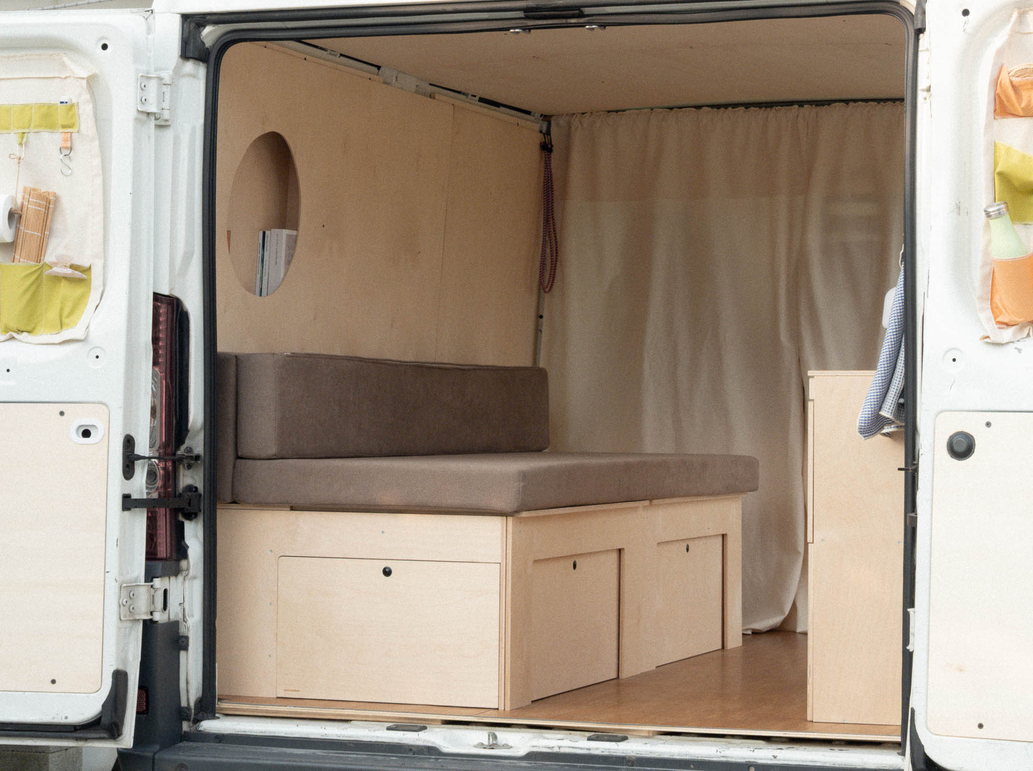 Letto Nom Outdoor in posizione divano con ante chiuse, sistema modulare per camperizzazione van con vano di stivaggio integrato e configurazione trasformabile