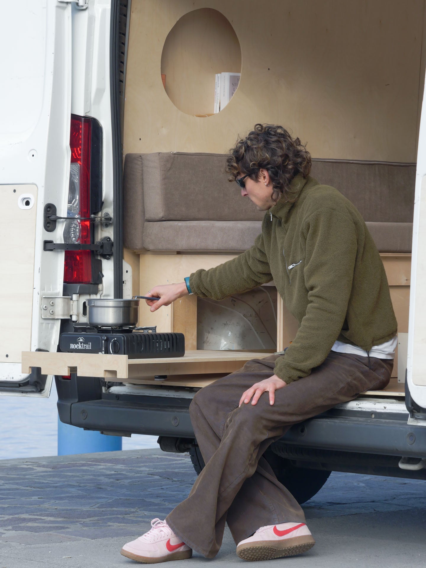 Persona che cucina con il Totem Cook posizionato sul piano estraibile laterale del van, sistema modulare per camperizzazione van con cucina outdoor integrata.