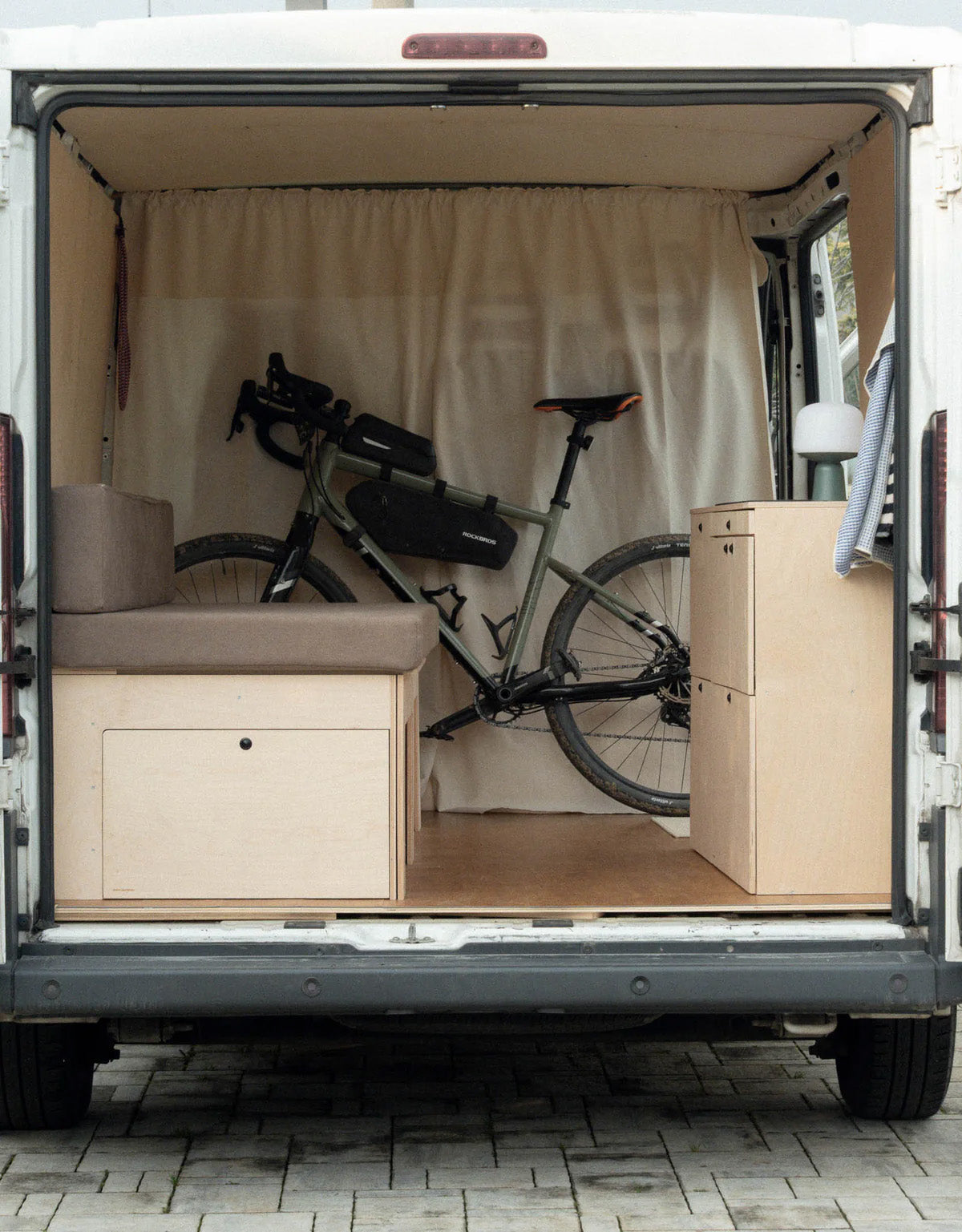 Nom Starter Kit installato nel van con spazio dedicato alla bicicletta dietro il letto modulare, soluzione per camperizzazione van ideale per appassionati di bici