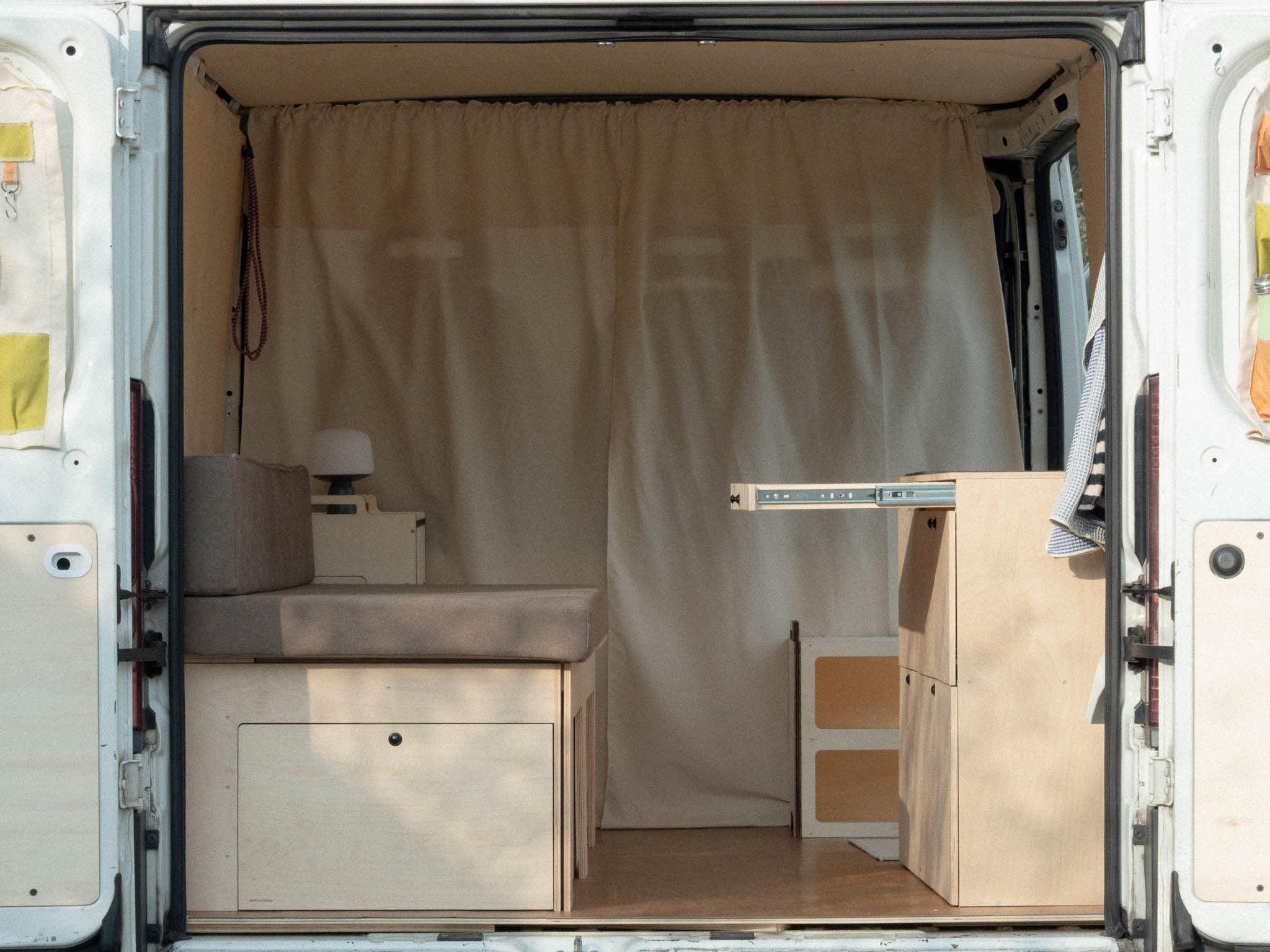 Vista laterale del Nom Total Kit installato nel van con tavolo estraibile aperto, soluzione completa per camperizzazione van modulare e allestimento funzionale